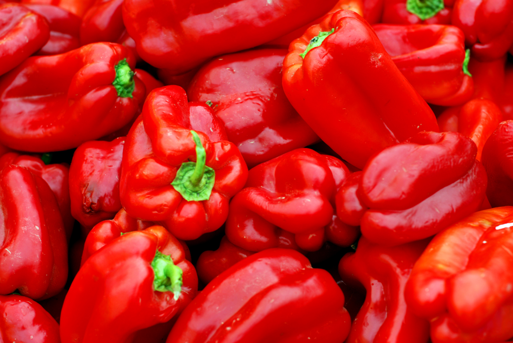 Fresh red, yellow, and green bell peppers piled high at a produce stand