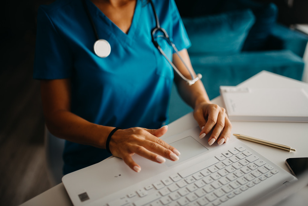 A clinician in scrubs working at a laptop